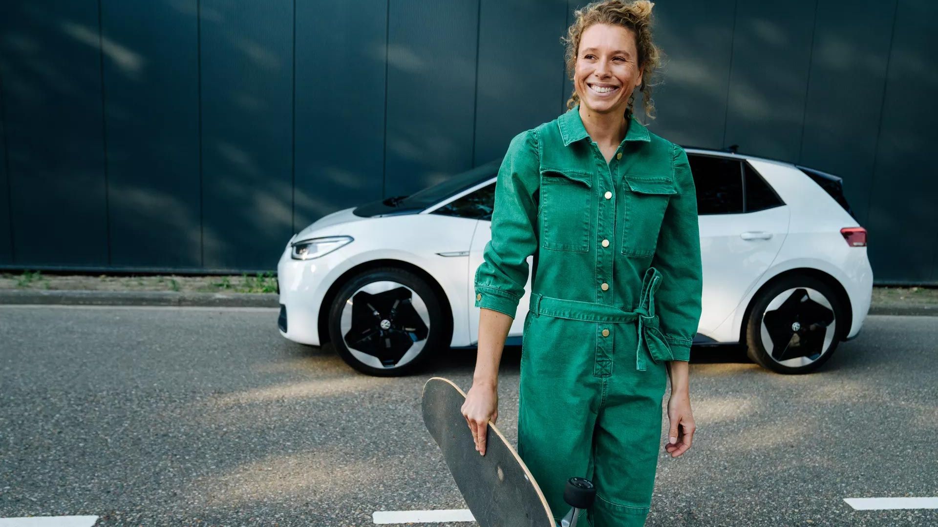 Frau mit Skateboard vor Elektroauto